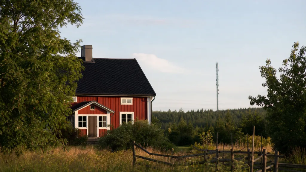 Rött hus i svensk glesbygd med mobilmast i fjärran