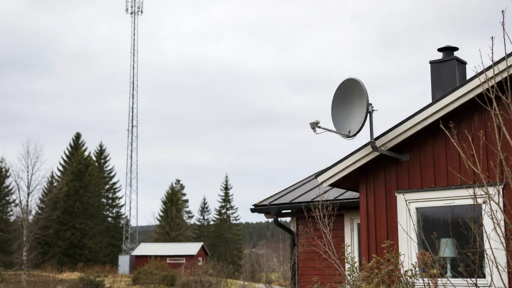 Satellitparabol och mobilmast vid ett rött hus i svensk glesbygd